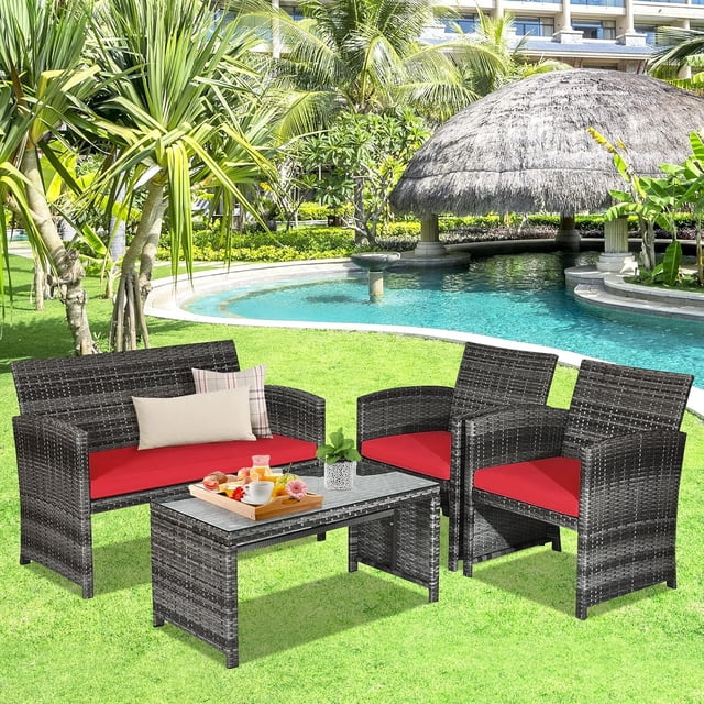 Gymax 4PCS Patio Outdoor Rattan Conversation Furniture Set with red cushions, including two single sofas, one loveseat, and a coffee table with tempered glass top. Ideal for outdoor spaces like patios, gardens, or poolside areas, surrounded by greenery and palm trees.