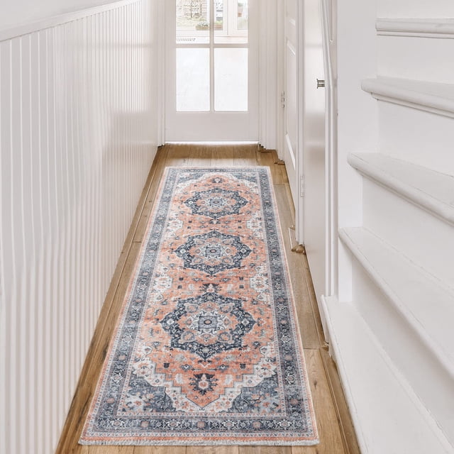 BY COCOON 2'x6' runner rug displayed in a hallway with a wooden floor and white walls. The rug features an intricate medallion pattern in shades of orange, blue, and white, with a low pile thickness of 0.2 inches. Made in Turkey with durable, non-slip, and stain-resistant cotton and chenille materials, it is washable and suitable for high-traffic areas like entryways, kitchens, and hallways. The rug protects delicate flooring and is kid and pet-friendly.