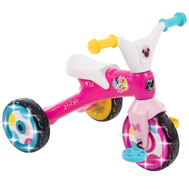 Disney Minnie Electro-Light Trike for Girls, pink preschool tricycle with white seat, yellow and blue handle grips, Minnie Mouse graphics, LED-lit colorful wheels, underseat storage, and stable three-wheel design for beginner riders.