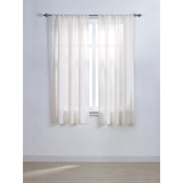 Mainstays Tille 63" solid rod pocket window curtains panel in white, hanging on a metal rod over a window with light gently filtering through the sheer 100% polyester fabric, enhancing privacy in a room with light wood flooring and pale walls, suitable for mixing with printed patterns for a customized look.
