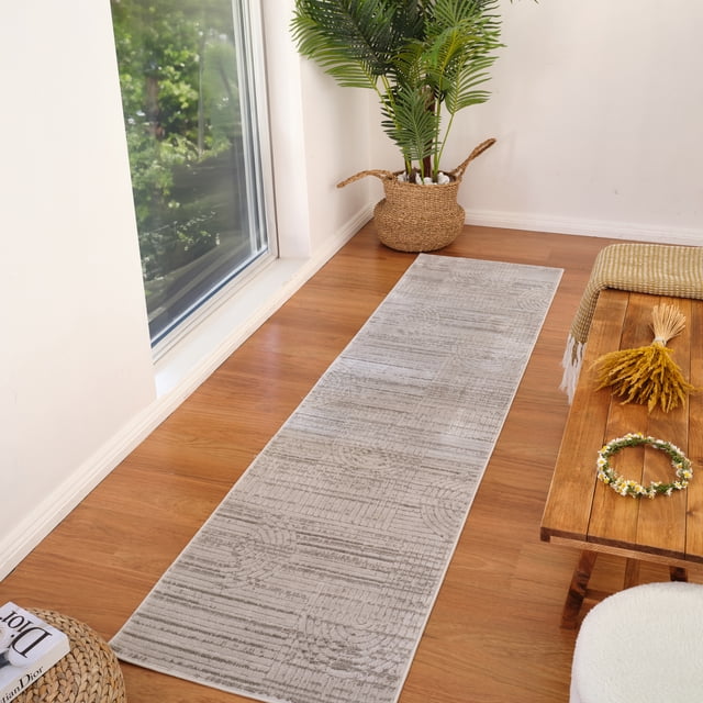 Rug Branch Astra Modern Indoor Area Rug in grey with geometric abstract design, 0.4-inch pile height runner on wood floor beside a large window, styled with a woven basket plant and wooden bench, suitable for hallways, entryways, and high-traffic indoor spaces.