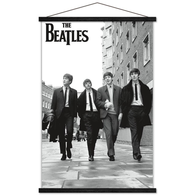 The Beatles - In London Wall Poster, 22.375" x 34" featuring a black and white photo of four men walking on a paved London street between brick buildings, dressed in 1960s suits and coats, with The Beatles logo in bold black letters at the top left, printed on glossy poster paper and hung with a black wooden frame, suitable for bedroom, office, or dorm wall decor.