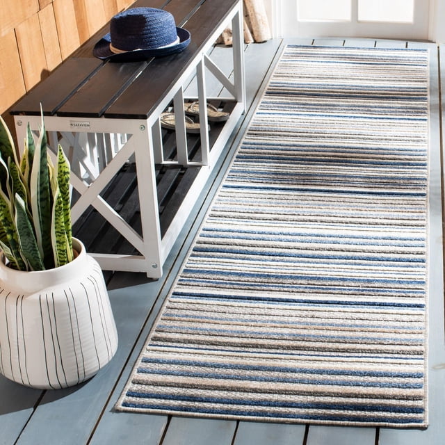 Safavieh Cabana Siomha Striped Outdoor Area Rug with horizontal blue, beige, and gray stripes, made of durable synthetic yarns for weather and sun resistance, placed on a light gray wooden floor next to a white and dark brown wooden bench with a blue hat and a white planter with snake plants, suitable for outdoor patios, porches, or indoor high-traffic areas.