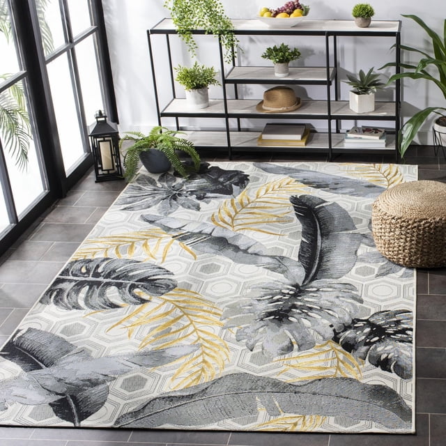 SAFAVIEH Barbados Tropical Leaves Outdoor Area Rug with a hexagonal geometric background and large tropical leaves in grey and yellow, placed on a tiled floor near a black metal shelving unit with potted plants and decor, suitable for enhancing outdoor patio spaces.