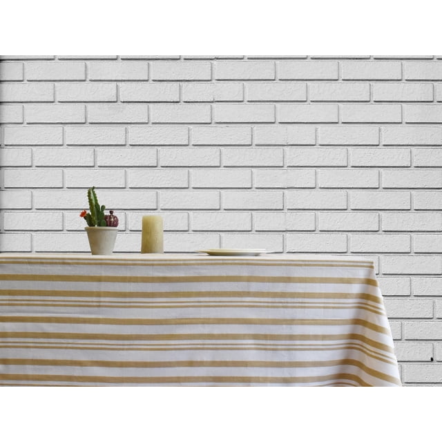 Fabstyles Broadway 100% Cotton Stripe Table Cloth in beige and white horizontal stripes on a rectangular table, featuring a small potted cactus, a beige candle, and a white plate, set against a white brick wall, ideal for dining and entertaining.