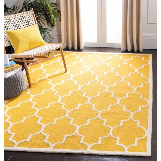 Safavieh Cambridge Kevin Geometric Area Rug in yellow with a white geometric trellis pattern, hand-tufted wool construction from the Cambridge Collection, displayed on dark hardwood floors with a woven chair and yellow cushion, ideal for home or office accent.